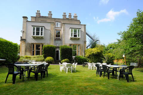 White plastic tables, and a mixture of white and black plastic chairs set out on a lawn at the back of a venue.