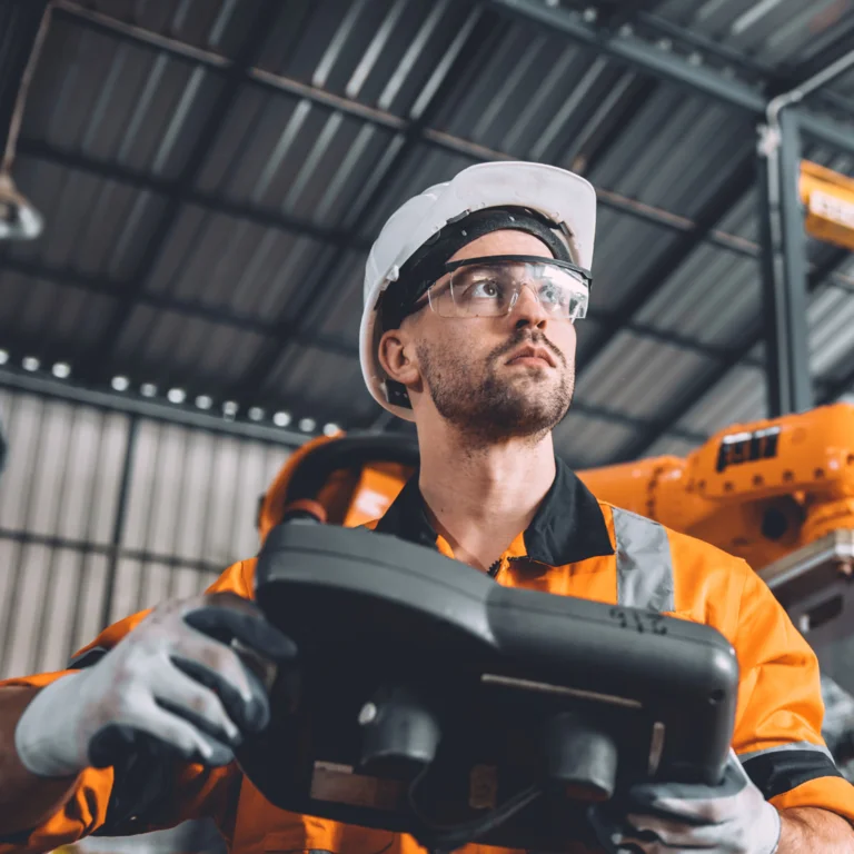 Industrial operator in orange hi-vis gear handling heavy machinery with precision, exemplifying CDM safety standards in an engineering environment